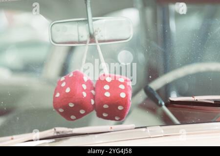 Due dadi rosa sfocati con puntini bianchi sono appesi allo specchietto retrovisore di un'auto d'epoca Foto Stock