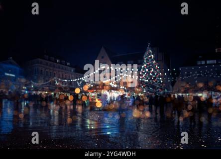 Immagine sfocata di una strada della città di notte con un albero di Natale sullo sfondo. La scena è vivace e festosa, con persone che camminano e si divertono Foto Stock