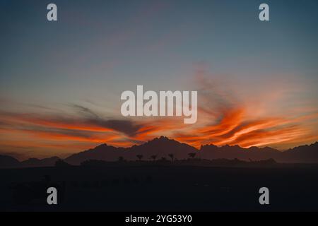 Il sole serale tramonta prima della montagna con il turbinio di nuvole all'orizzonte. Silhouette di palme. Foto Stock