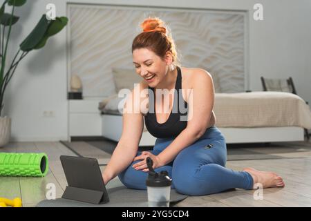 Allenamento di yoga fitness online. Donna che pratica stretching con lezioni online di app a casa. In più, una donna che fa esercizio sportivo su un tappetino da yoga al coperto. La ragazza ha un allenamento per la perdita di peso Foto Stock