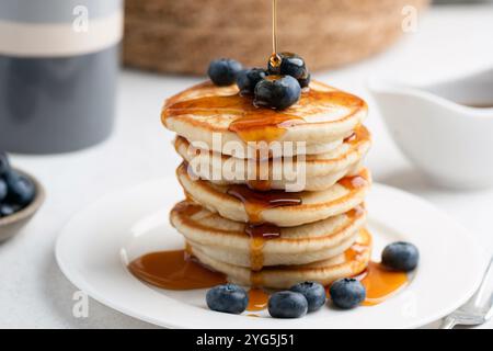 Sciroppo d'acero che versa sui pancake. Pila di soffici pancake al siero di latte con mirtilli, vista ravvicinata Foto Stock