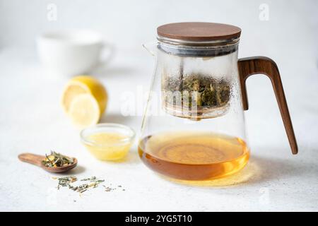 Teiera in vetro con tè al limone alle erbe su sfondo grigio chiaro in pietra. Detergere, disintossicare Foto Stock