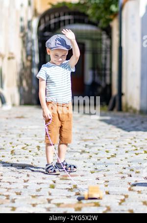 Un bambino con un giocattolo di legno si dirige verso la macchina fotografica in una strada estiva Foto Stock