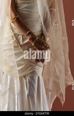 Drappeggiata da un abito bianco e eleganti perle, una bella donna irradia il suo fascino in un ambiente da studio. Foto Stock