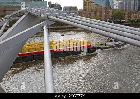 Vista della chiatta trainante del rimorchiatore con container gialli sotto il Millennium Bridge nella città di Londra Inghilterra Regno Unito 2024 KATHY DEWITT Foto Stock