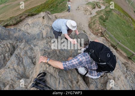 Due arrampicatori che stringono le mani per sostenersi l'un l'altro mentre salgono la vetta rocciosa di Cat Bells in Cumbria Foto Stock