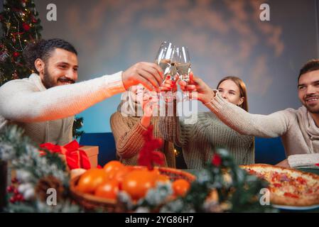 Gli amici brindano con flute di champagne alla vigilia di Natale con pizza e mandarini Foto Stock