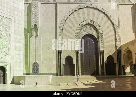 Madre, figlia e figlio giocano vicino alle imponenti mura della Moschea Hassan II a Casablanca, in Marocco, mostrando la splendida architettura della moschea Foto Stock