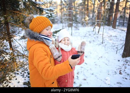 Un fratello e una sorella sono gioiosamente impegnati in una videochiamata, sullo sfondo mozzafiato di una foresta innevata. La scena cattura le loro risate e. Foto Stock