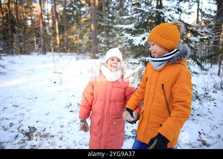 Un fratello e una sorella camminano insieme gioiosamente attraverso una tranquilla foresta innevata, circondata da alti alberi ricoperti di bianco. Foto Stock