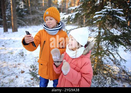 Un fratello e una sorella sono gioiosamente impegnati in una videochiamata, sullo sfondo mozzafiato di una foresta innevata. La scena cattura le loro risate e. Foto Stock