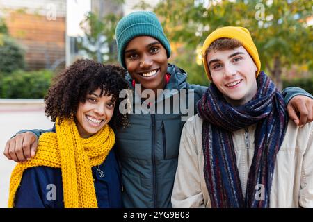 Tre giovani e diversi amici sorridenti alla macchina fotografica in piedi insieme all'aperto Foto Stock