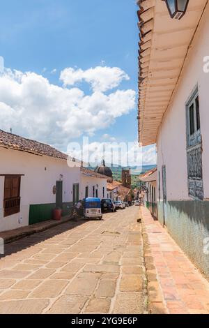 Barichara, Santander, Colombia, 11 ottobre 2024. Immagine verticale di una strada acciottolata, con la cupola e una torre della cattedrale visibili nella ba Foto Stock