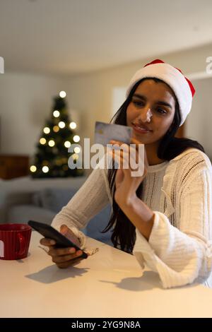 Natale, donna asiatica a Babbo cappello shopping online con smartphone e carta di credito, a casa Foto Stock