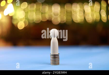 Bambola di legno su una pila di monete. Concetto di successo finanziario. Sfondo bokeh Foto Stock