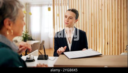 Persone, clienti e addetti alla reception dell'hotel con appunti, informazioni sulle prenotazioni e checklist al banco. Help desk, ospitalità e portineria con Foto Stock