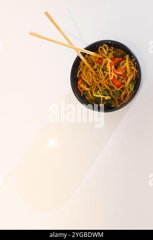 Bacchette appoggiate su un piatto di colorati spaghetti saltati con verdure, spazio per copiare, a casa Foto Stock