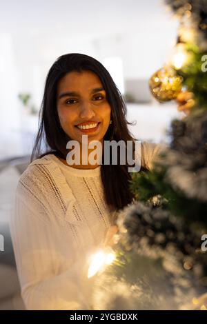 Donna sorridente che decora l'albero di Natale a casa, godendo dello spirito festivo Foto Stock