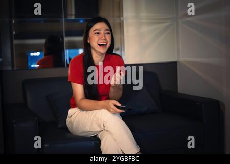 Donna divertente che guarda la TV su un divano la sera Foto Stock