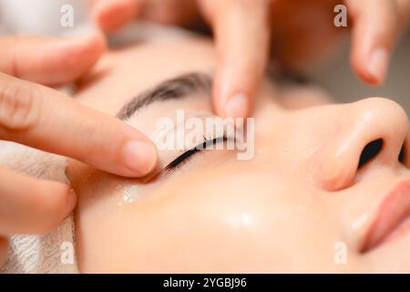 Trattamento delle palpebre. Clinica anti-invecchiamento donna occhi chiusi con gel di trattamento della palpebra superiore procedura. Massaggiatrice massaggiatrice massaggiando delicatamente il viso e gli occhi del cliente Foto Stock