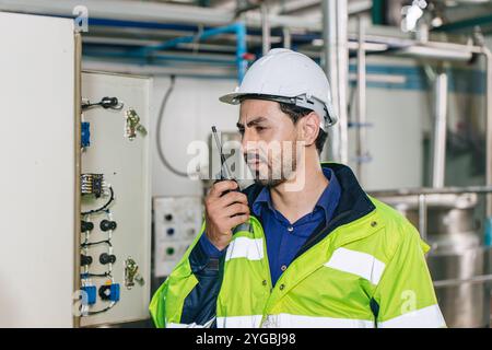 Ingegnere in servizio, lavoratore latino maschio in fabbrica in una centrale elettrica a gas e petrolio con controllo, gestisce l'ordine con comunicazione walkie-talkie al lavoro Foto Stock