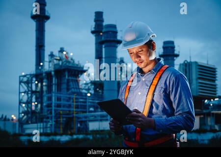 Ingegnere del turno di notte, servizio di raffineria di petrolio e gas, lavoratore di sesso maschile, duro lavoro negli impianti dell'industria petrolifera, sfondo scuro. Foto Stock