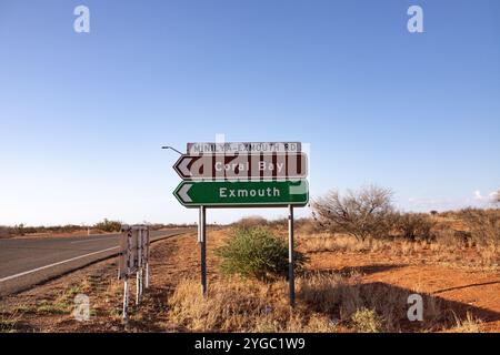 Segnaletica stradale marrone e verde con direzione verso il cielo blu nella sporcizia rossa dell'Outback sul lato della strada, che indica la strada per Coral Foto Stock