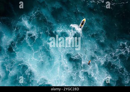 Moto d'acqua e surfista in azione, surf trainato in mezzo al mare blu profondo con acqua torbida, schiuma marina e spruzzi. Drone aereo sparato da una vista dall'alto Foto Stock