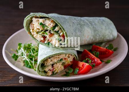 Il burrito si avvolge con omelette all'uovo strapazzate e verdure nel piatto di pane pita verde. Primo piano Foto Stock