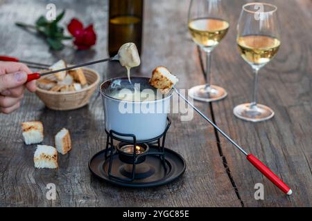 Fonduta con gustoso formaggio fuso, forchette, pane e vino su un tavolo di legno, primo piano Foto Stock