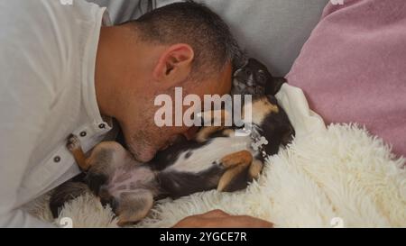 Uomo ispanico di mezza età accoccolato con due cani chihuahua su un comodo divano in un salotto di casa. Foto Stock