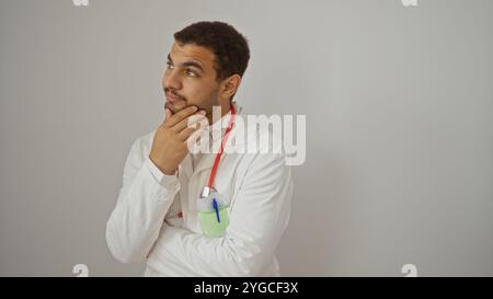 Giovane ispanico in cappotto medico e stetoscopio pensando su sfondo bianco isolato Foto Stock