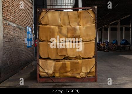 Durante il processo di produzione, i fogli di gomma naturale sono stati asciugati all'aria su un binario di acciaio appeso vicino alla parete in mattoni della fabbrica. Foto Stock