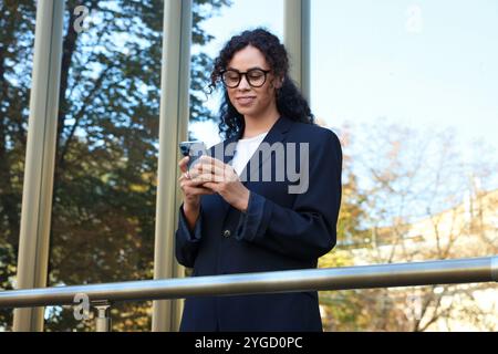 Ritratto di una giovane donna con un telefono che indossa un'elegante tuta all'aperto Foto Stock