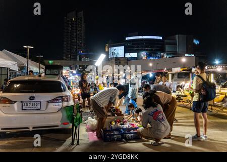 Adulti e bambini sono visti alla ricerca di merci in una bancarella di giocattoli vintage a terra al Green Vintage Market di Ratchayothin, Bangkok, con moderni grattacieli sullo sfondo. Il Green Vintage Market di Ratchayothin, Bangkok, è un mercato all'aperto noto per il suo eclettico mix di prodotti d'epoca e artigianato. Con la sua atmosfera bohémien, il mercato presenta anche una sezione specializzata in giocattoli vintage e da collezione, dove collezionisti di giocattoli e appassionati possono trovare rare action figure, modellini di auto, bambole classiche, statuette anime e altri tesori nostalgici. Foto Stock