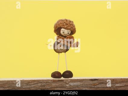 Figura di castagno con cappello e sciarpa davanti allo sfondo giallo nello studio Foto Stock