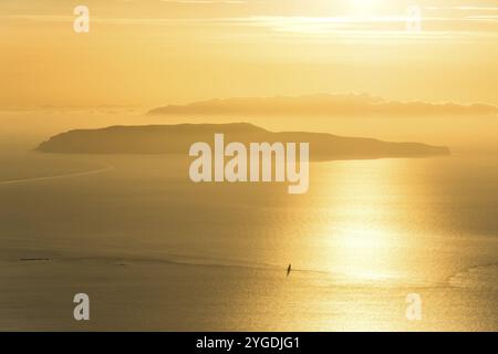 Piccola isola e barca solitaria a vela sull'oceano durante il tramonto spettacolare dorato Foto Stock