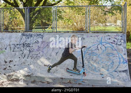 Bambino su kick scooter nel parco. I ragazzi imparano a rullo di skate board. Little Boy pattinaggio sulla soleggiata giornata estiva. Attività all'aperto per i bambini sulla sicurezza residen Foto Stock