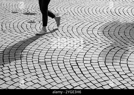 Piedi e gambe di una persona che cammina su strade acciottolate Foto Stock