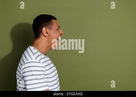 Foto ritratto di un bel giovane ragazzo profilo urla vestito arrabbiato elegante indumento bianco a righe isolato su sfondo color cachi Foto Stock