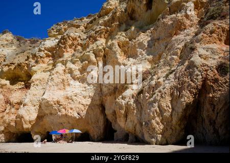 Ombrelloni colorati contro le torreggianti scogliere di Praia da Rocha Foto Stock