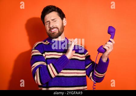 Giovane uomo in maglione a righe viola con telefono vintage su sfondo arancione Foto Stock