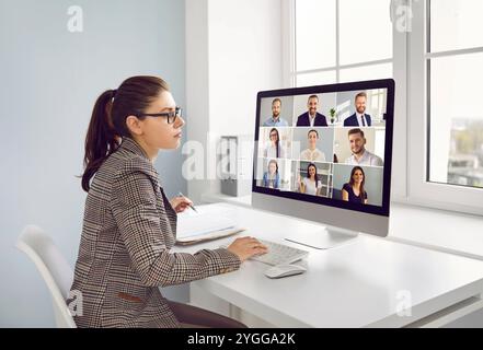 Giovane leader donna concentrata in ufficio che effettua videochiamate di lavoro con i compagni di squadra. Foto Stock