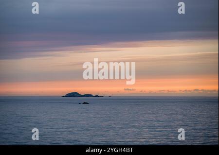 Basse rocce che emergono da un oceano calmo, al tramonto. Il sole è caduto all'orizzonte e il cielo è arancione Foto Stock