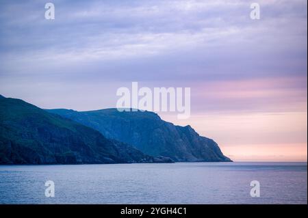 Il glorioso tramonto al largo della costa norvegese, visto dalla nave da crociera, mentre il sole illumina dolcemente la scogliera Foto Stock