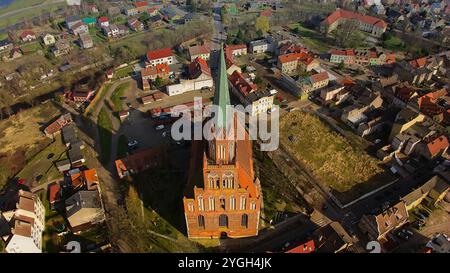 Un panorama nuvoloso su Trzebiatów, che cattura l'imponente guglia in mattoni rossi della chiesa gotica di 90 metri e il suo mix di edifici tradizionali e campi verdi Foto Stock