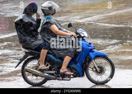 Una coppia di impermeabili sta guidando una moto sotto la pioggia, in Thailandia Foto Stock