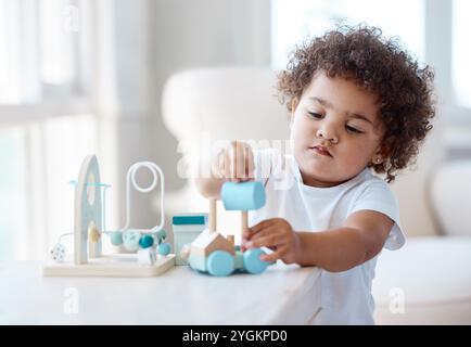 Giocattoli, giochi e baby by table in casa per la crescita, lo sviluppo e l'educazione all'asilo. Soggiorno, bambino e adorabile bambino con Foto Stock