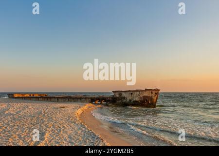 Lo scafo della nave dopo l'incidente, che si trova sulla riva. Un vecchio relitto giace su una spiaggia sabbiosa mentre il sole tramonta Foto Stock