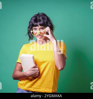 Allegro giovane studente di latina con un libro che guarda la macchina fotografica su sfondo verde - stile di vita della gente - ritratti in studio Foto Stock